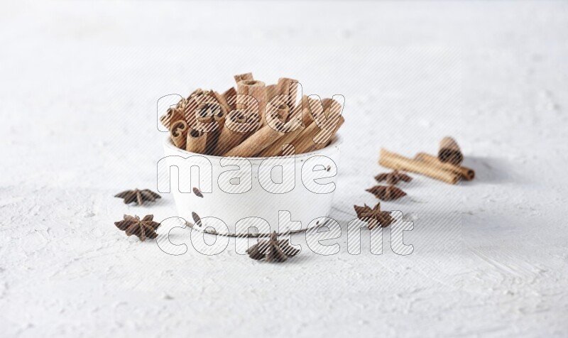 White bowl full of cinnamon sticks surrounded by star anis on a textured white background in different angles
