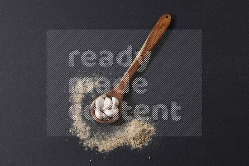 A wooden ladle full of garlic cloves with sprinkled powder on a black flooring