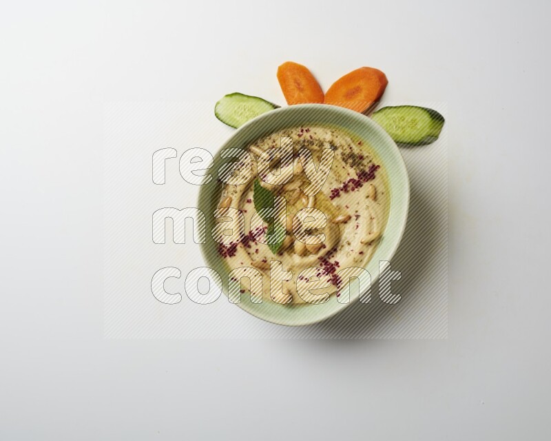 Hummus in a green plate garnished with zattar & sumak on a white background