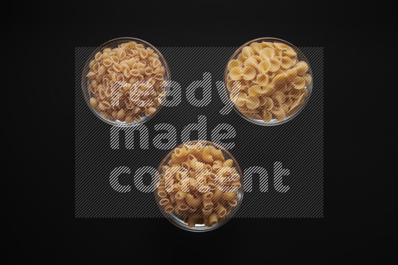 Different pasta types in glass bowls on black background