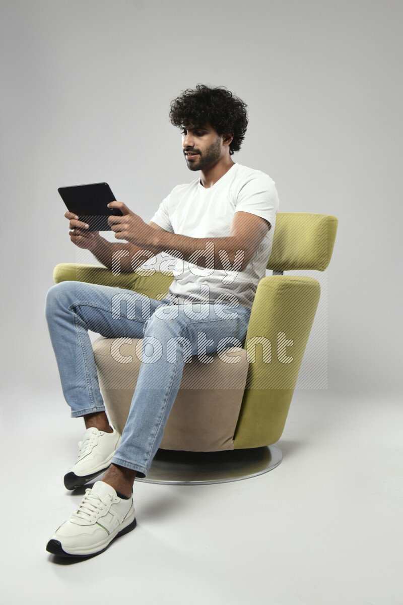 A man wearing casual sitting on a chair gaming on a tablet on white background
