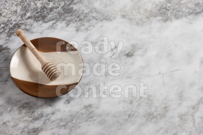 Multicolored pottery plate with wooden honey dipper in it on grey marble background