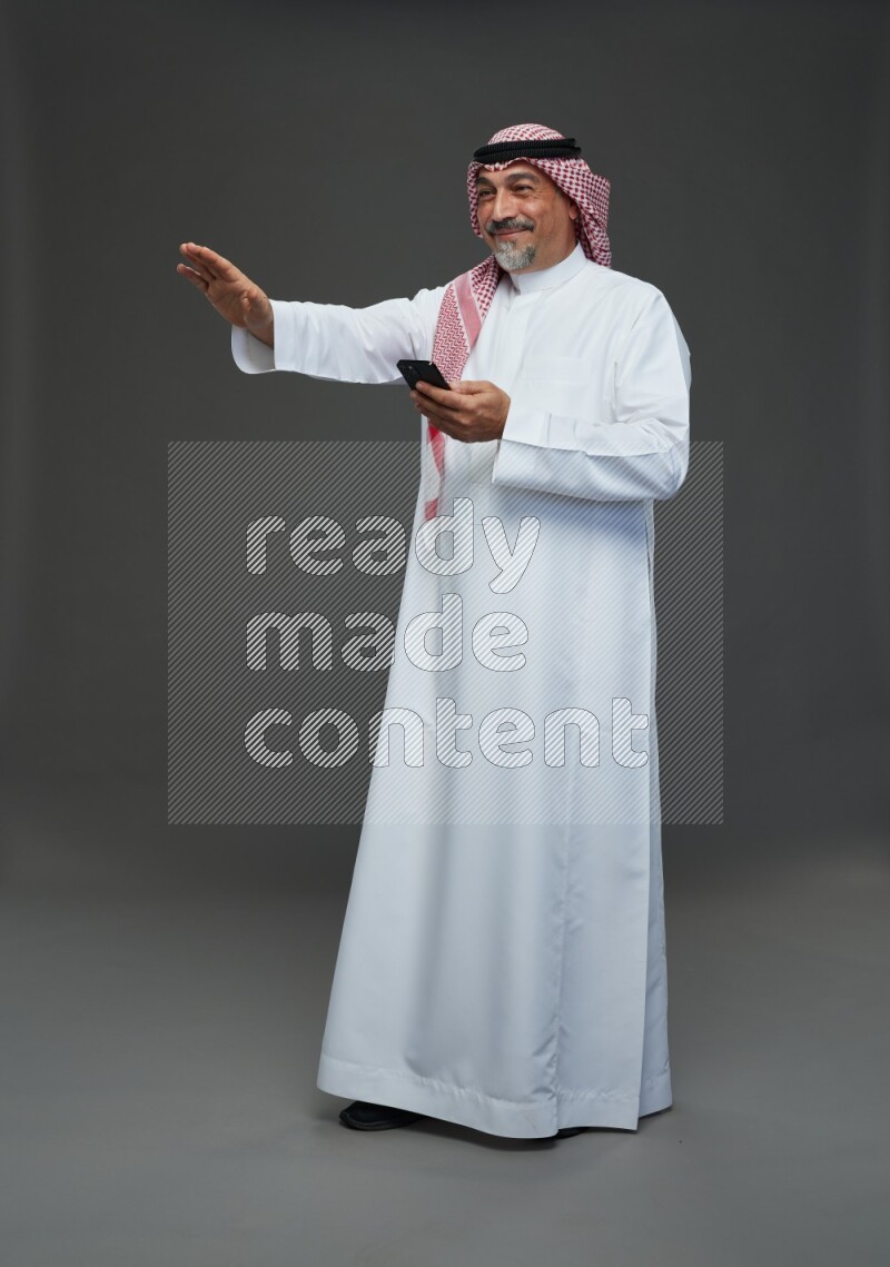 Saudi man with shomag Standing texting on phone on gray background