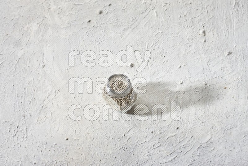 Herbal Glass jar full of white pepper beads on textured white flooring