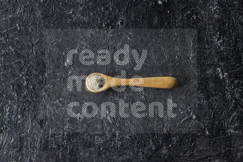 A wooden spoon full of white pepper powder on textured black flooring
