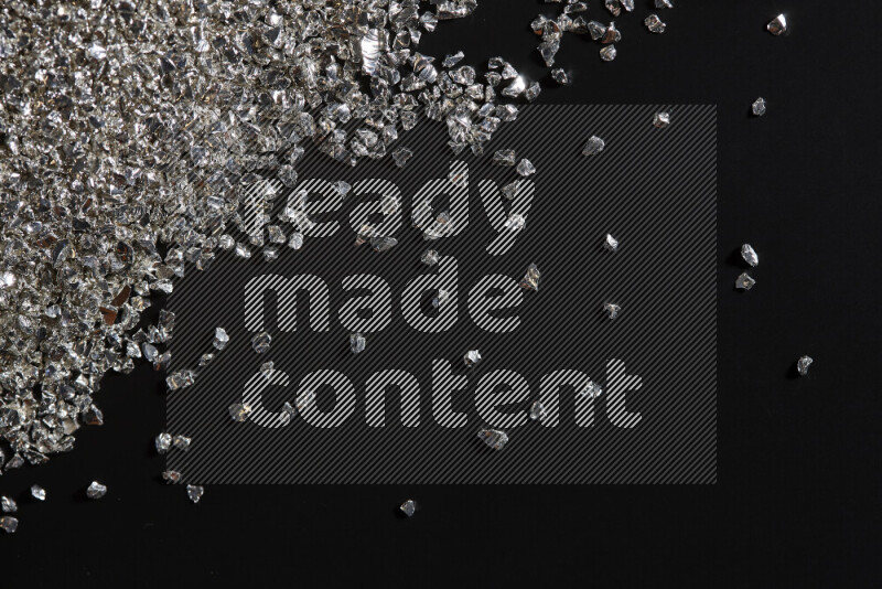 Silver shimmering fragments of glass scattered on a black background