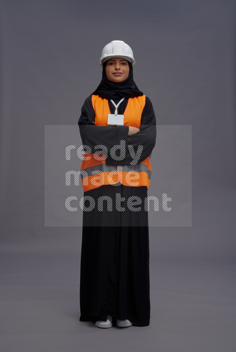 Saudi woman wearing Abaya with engineer vest with neck strap employee badge standing with crossed arms on gray background