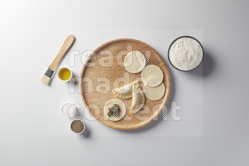 two closed sambosas and one open sambosa filled with meat while flour, salt, black pepper and oil with oil brush aside in a wooden dish on a white background