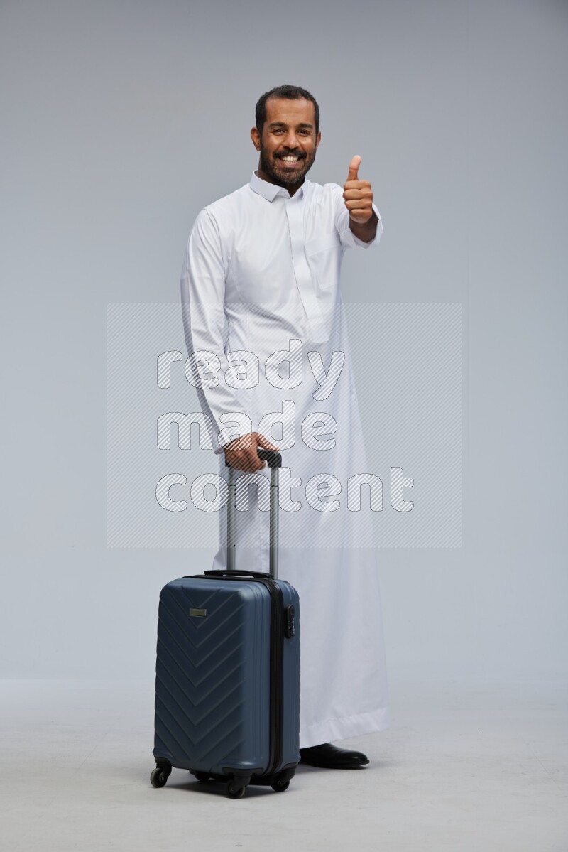 Saudi man wearing thob standing holding Travel bag on Gray background