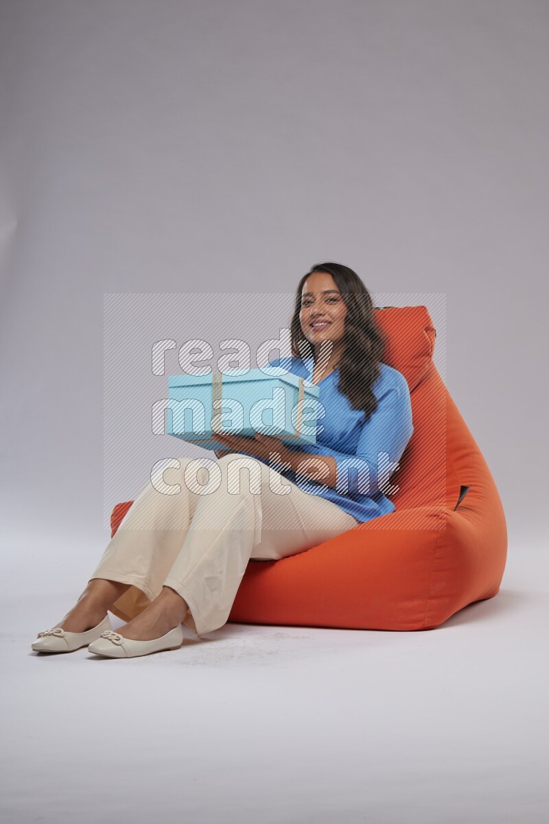 A woman sitting on an orange beanbag and opining a gift