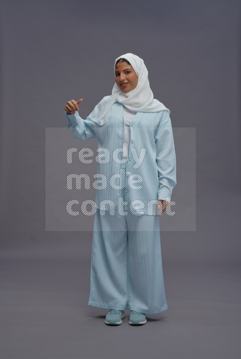 Saudi woman wearing hijab clothes standing interacting with the camera on gray background