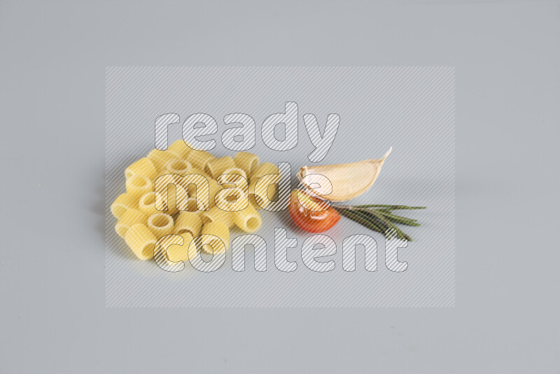 Raw pasta with different ingredients such as cherry tomatoes, garlic, onions, red chilis, black pepper, white pepper, bay laurel leaves, rosemary, cardamom and mushrooms on light blue background