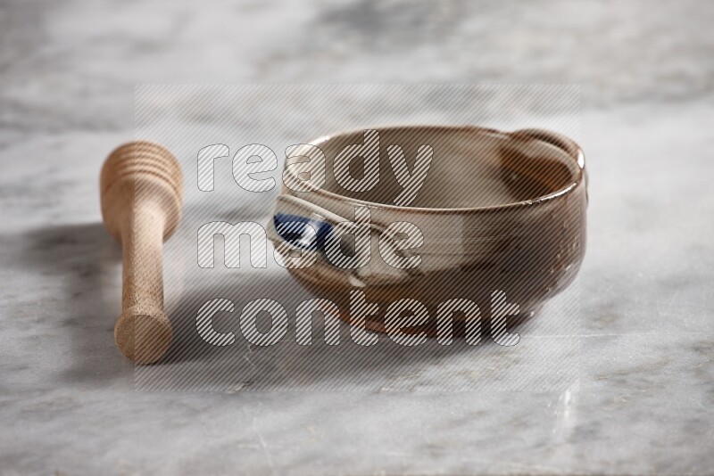 Multicolored pottery bowl with wooden honey dipper on the side on grey marble background