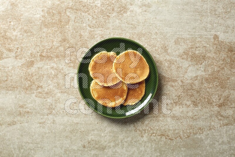 Four stacked plain mini pancakes in a green plate on beige background