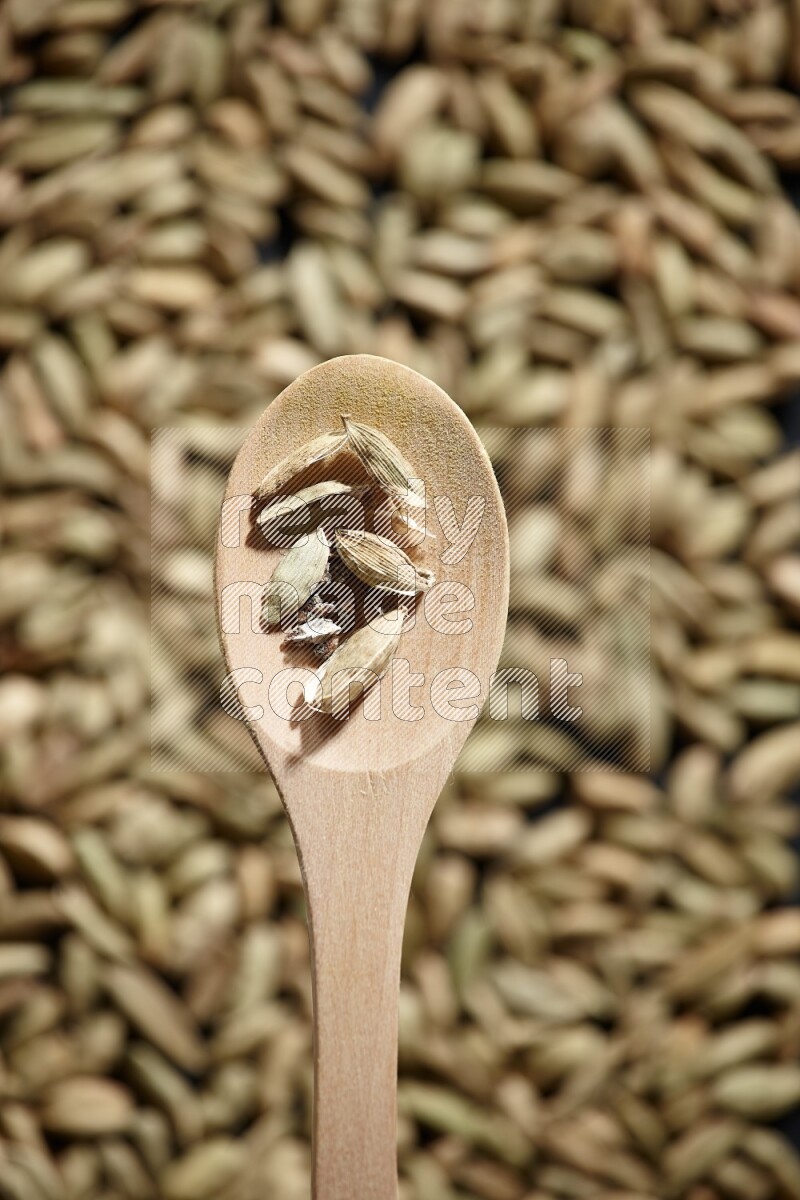 Cardamom seeds in a wooden spoon above cardamom seeds background on black flooring