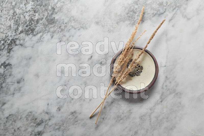 Wheat stalks on decorative pottery plate on grey marble background