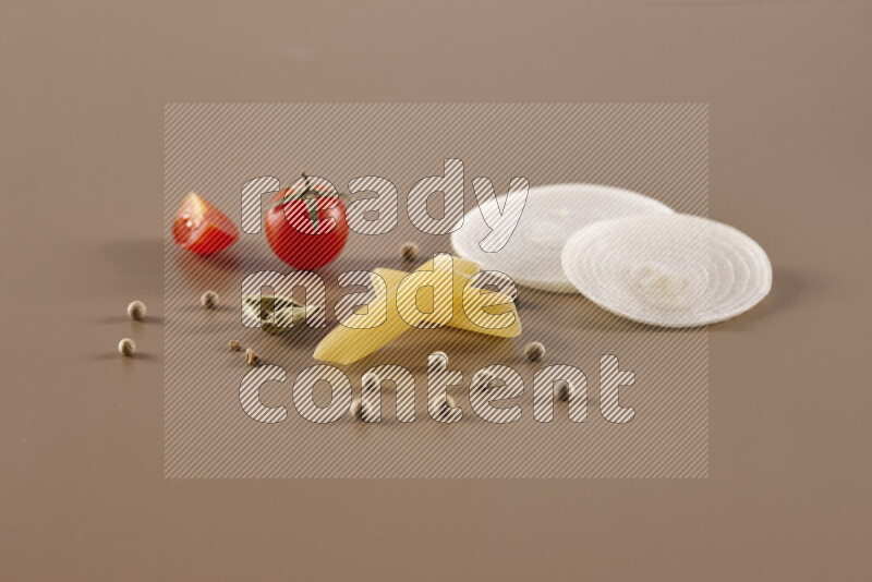 Raw pasta with different ingredients such as cherry tomatoes, garlic, onions, red chilis, black pepper, white pepper, bay laurel leaves, rosemary and cardamom on beige background