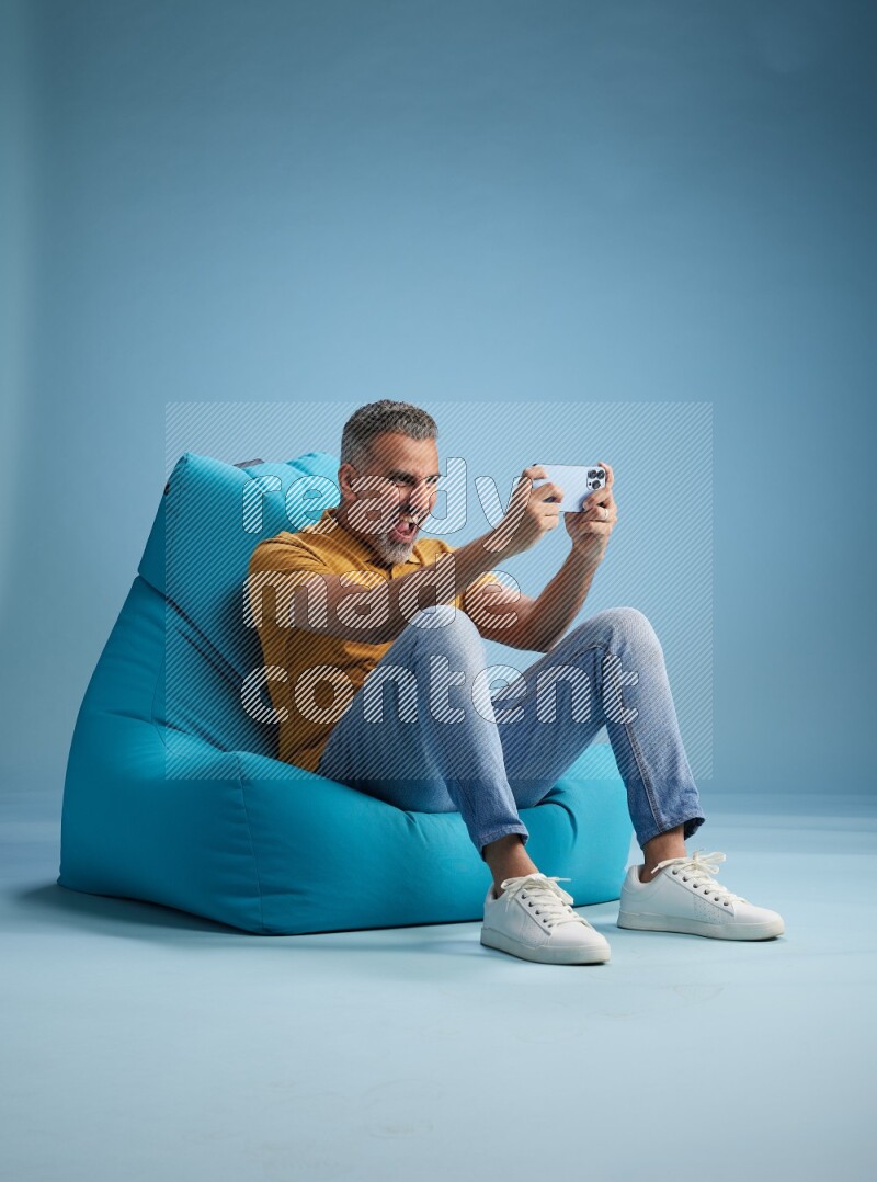 A man sitting on a blue beanbag and playing on phone