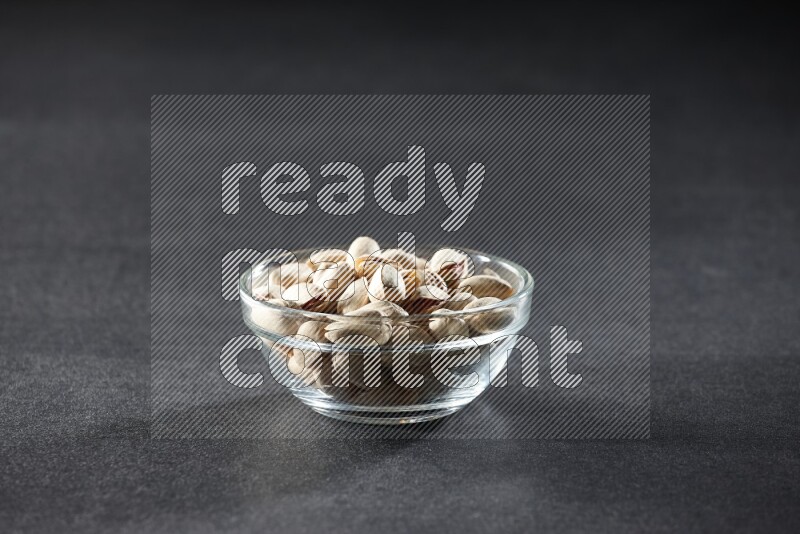 A glass bowl full of pistachios on a black background in different angles