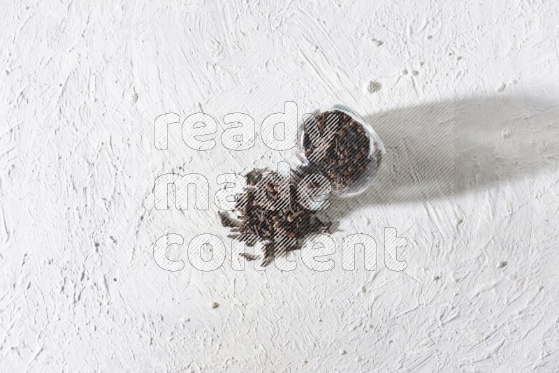 A flipped glass spice jar full of cloves and cloves came out of it on textured white flooring