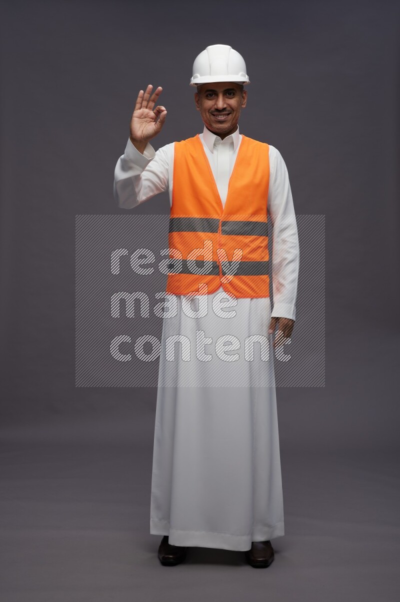 Saudi man wearing thob with engineer vest standing interacting with the camera on gray background