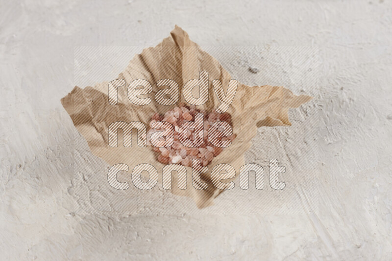 A crumpled piece of paper full of pink himalayan salt on white background