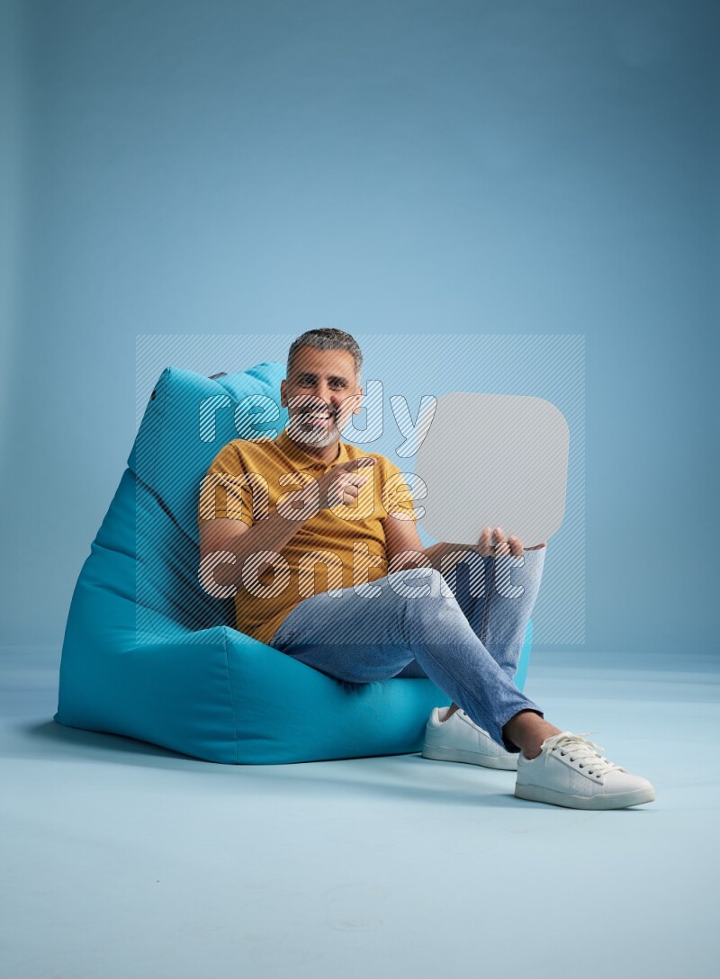 A man sitting on a blue beanbag and holding social media sign