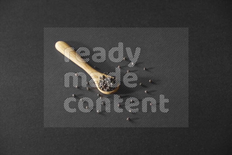 A wooden spoon full of black pepper on a black flooring