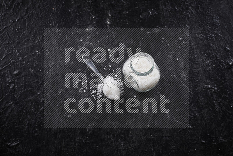 A glass jar full of coarse sea salt crystals on black background