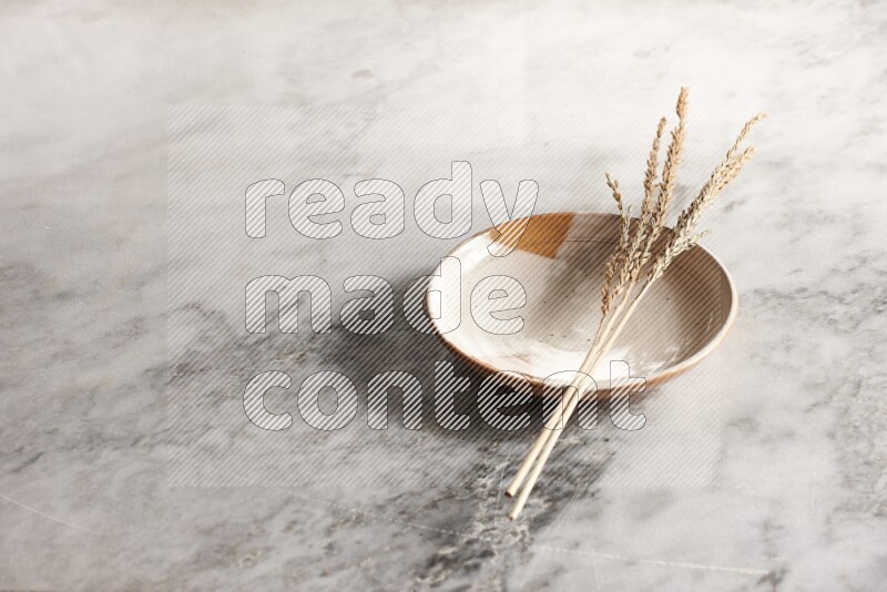 Wheat stalks on multicolored pottery plate on grey marble background