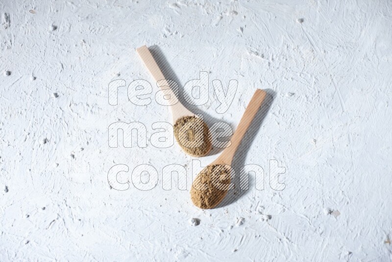 Wooden spoons full of allspice powder and allspice whole balls spreaded on a textured white flooring