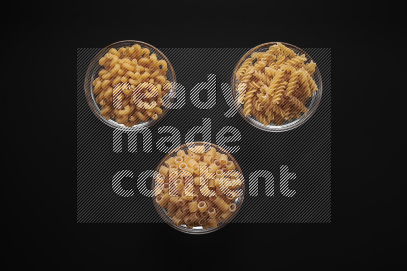 Different pasta types in glass bowls on black background