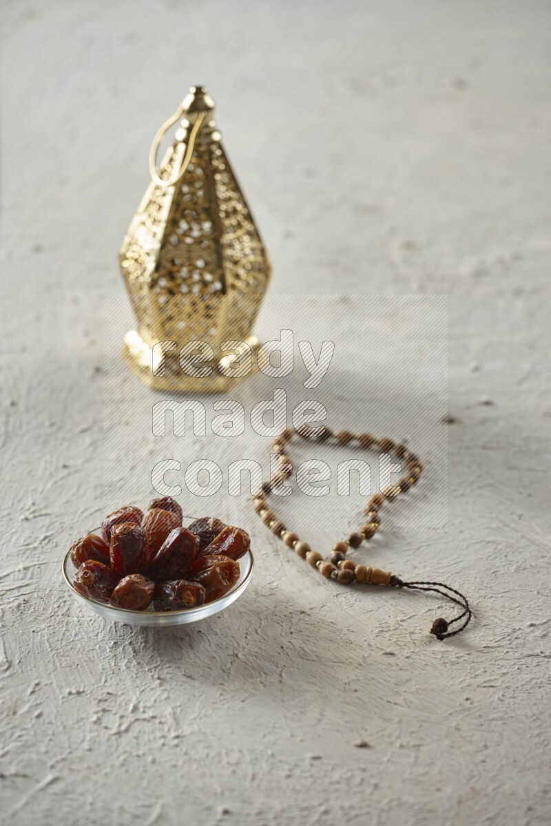 A golden lantern with different drinks, dates, nuts, prayer beads and quran on textured white background