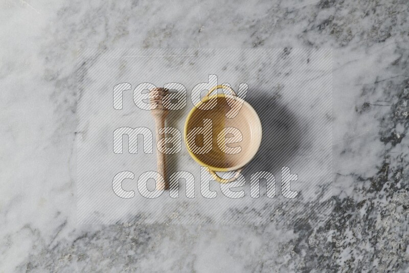 Multicolored pottery bowl with wooden honey dipper on the side on grey marble background