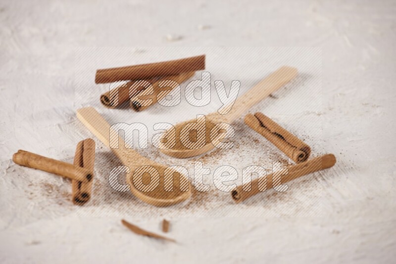 Two wooden spoons full of cinnamon powder with cinnamon sticks on white background