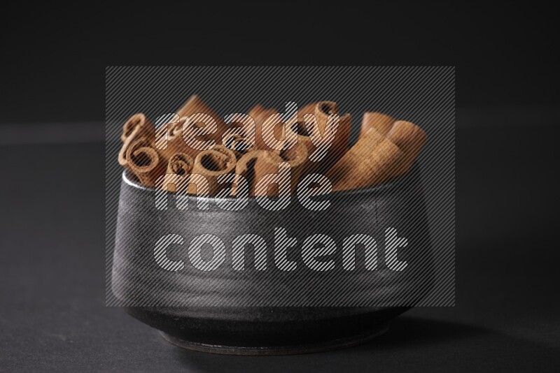 Cinnamon sticks in a black bowl on a black background in different angles
