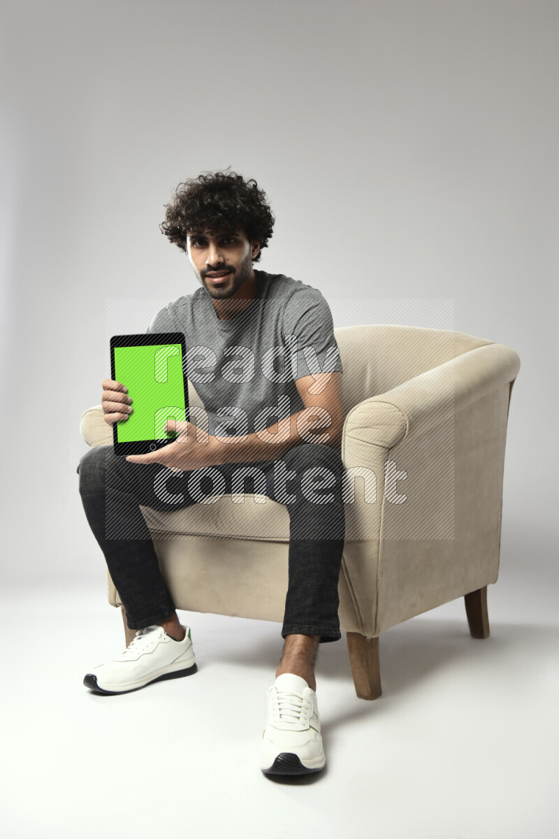 A man wearing casual sitting on a chair showing a tablet screen on white background