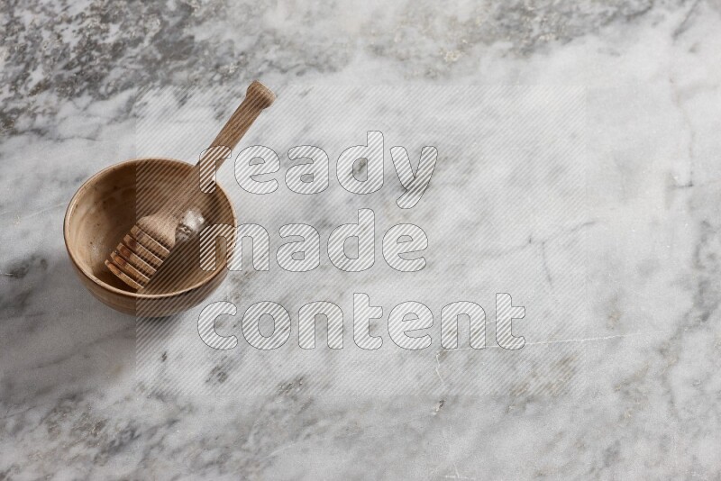 Beige pottery bowl with wooden honey dipper in it on grey marble background