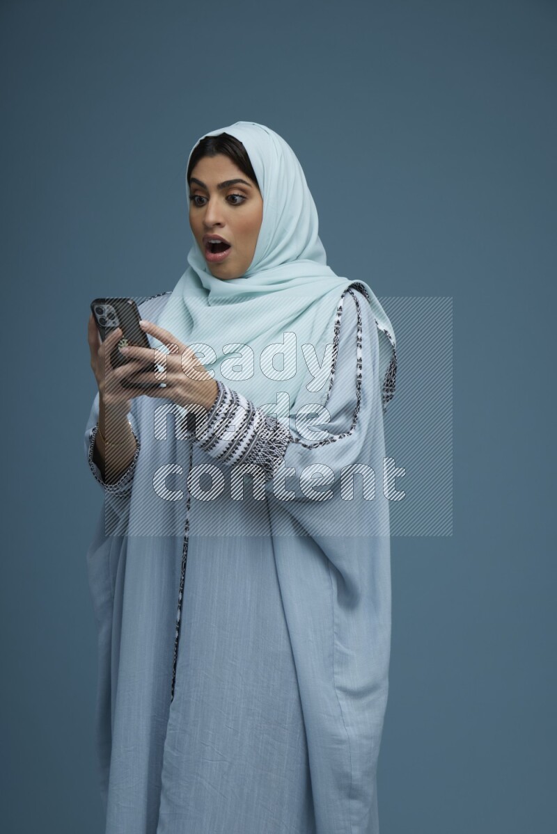 A Saudi woman Texting in a blue background wearing a blue Abaya with hijab