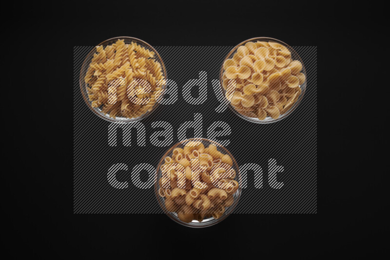 Different pasta types in glass bowls on black background