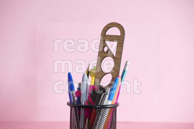 Pens, pencils and other different school supplies in a metal pen holder on rose background