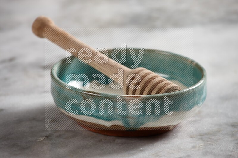 Multicolored pottery bowl with wooden honey dipper in it on grey marble background