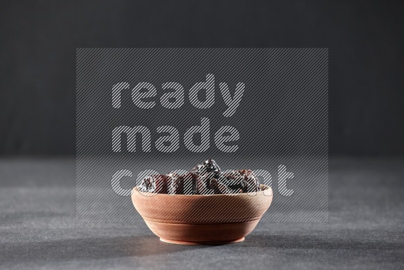 A wooden bowl full of dried plums on a black background in different angles