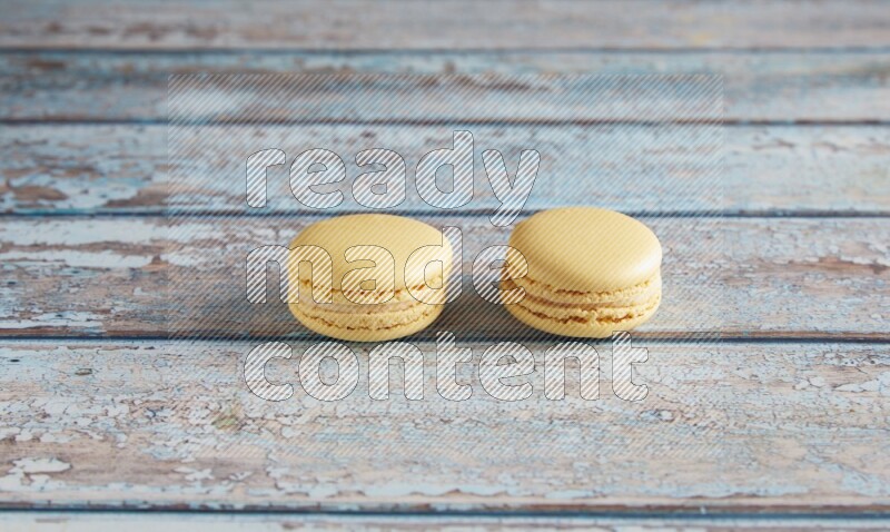 45º Shot of two Yellow Vanilla macarons on a light blue wooden background
