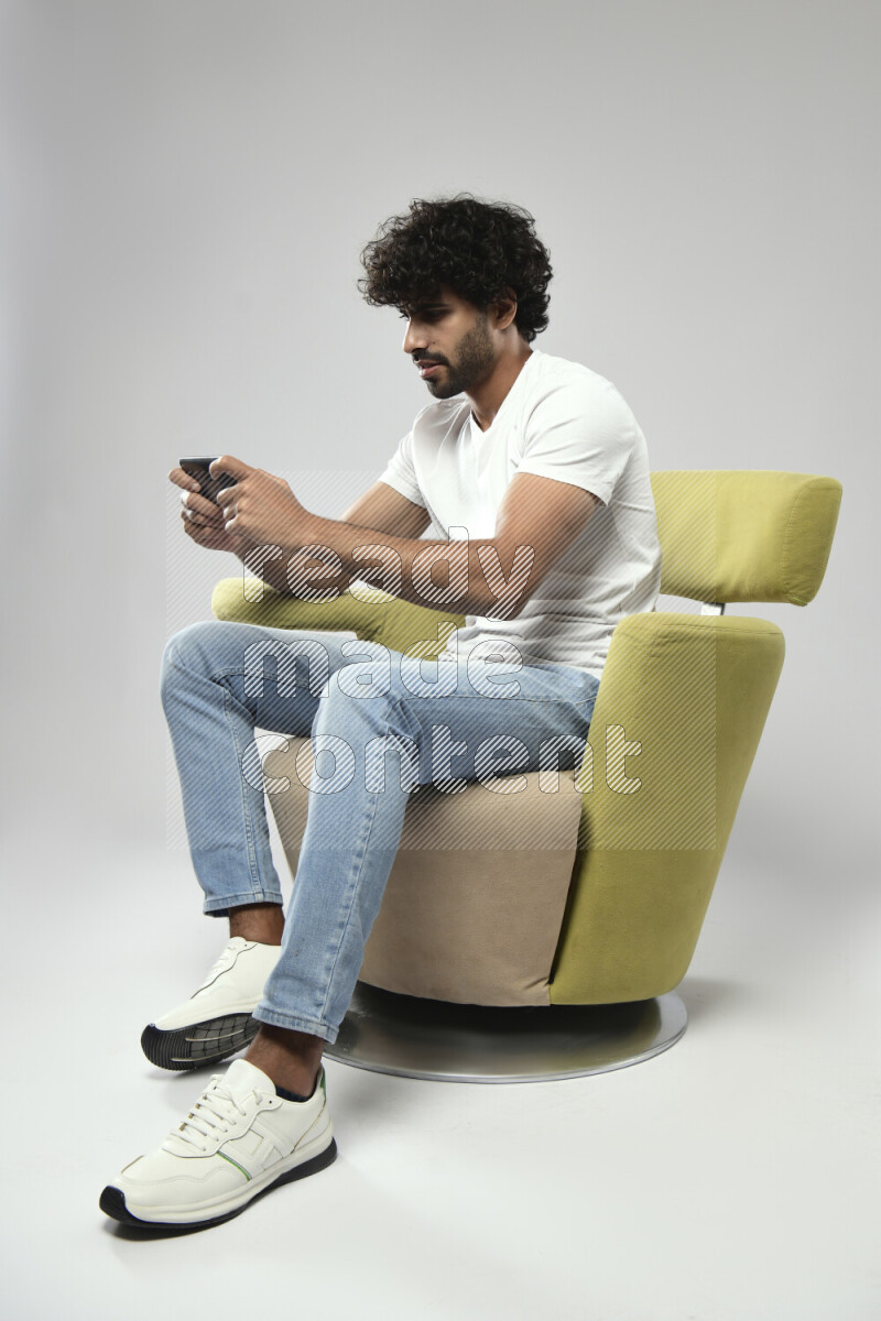 A man wearing casual sitting on a chair gaming on the phone on white background