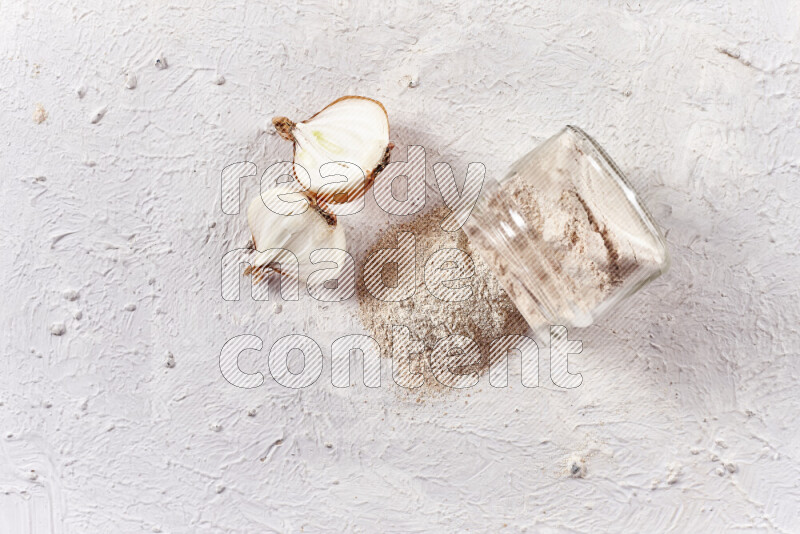 A glass jar full of onion powder flipped with some spilling powder on white background