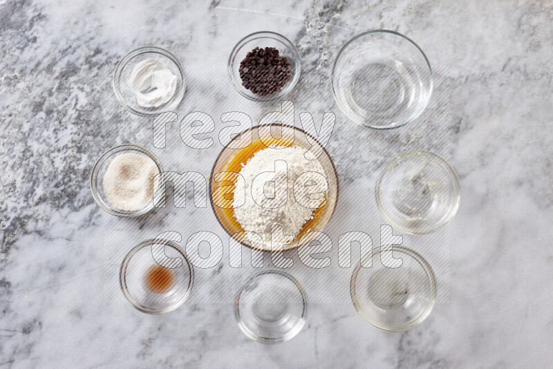 Cookies step by step with its ingredient, flour, butter, brown sugar, egg, vanilla extract, white sugar, chocolate chips and baking soda on grey marble background