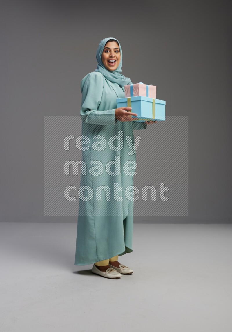 Saudi Woman wearing Abaya standing holding gift box on Gray background