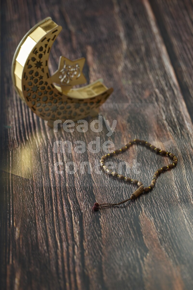 A wooden golden crescent lantern with different drinks, dates, nuts, prayer beads and quran on brown wooden background