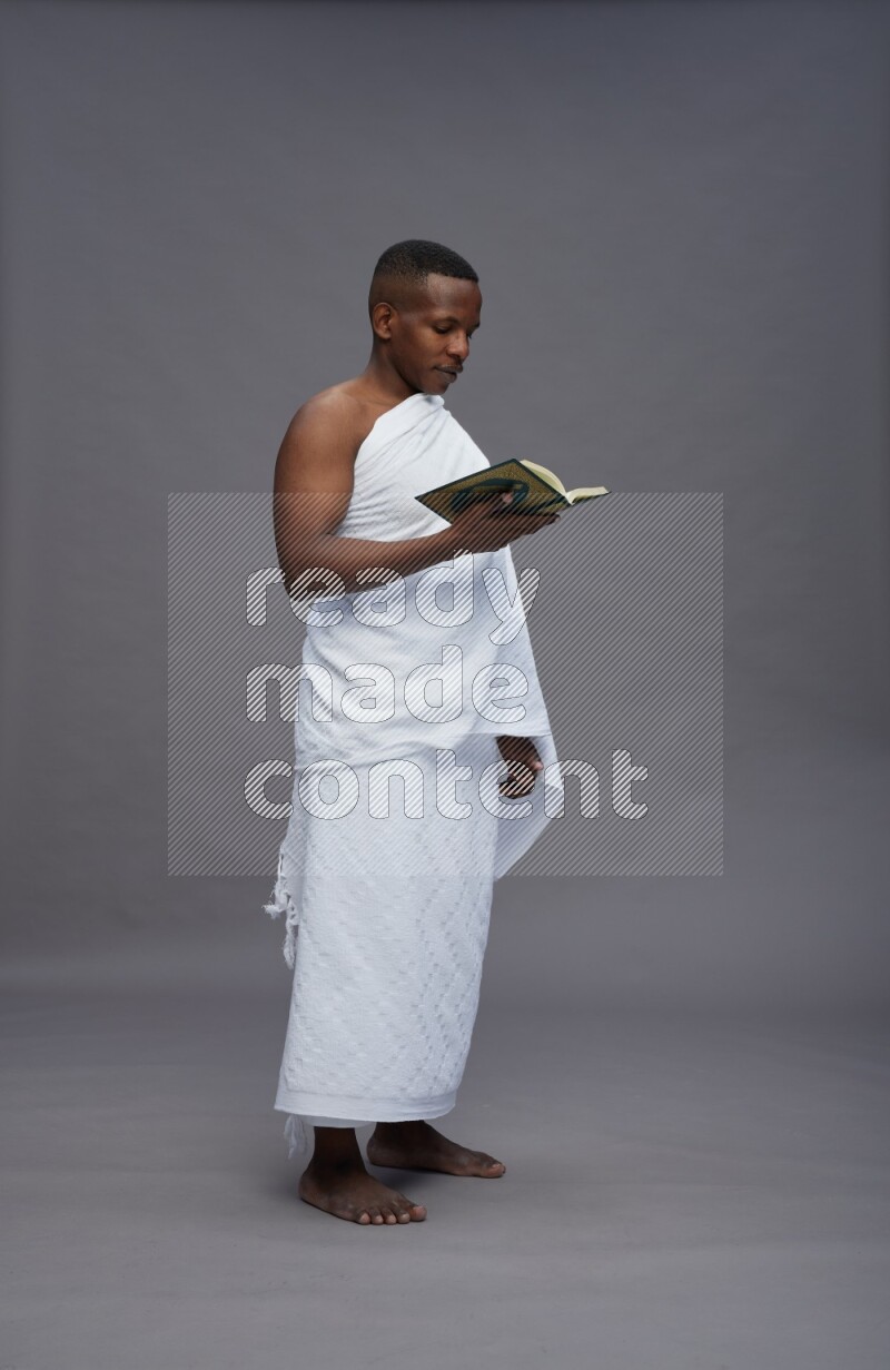 A man wearing Ehram Standing reading quran on gray background